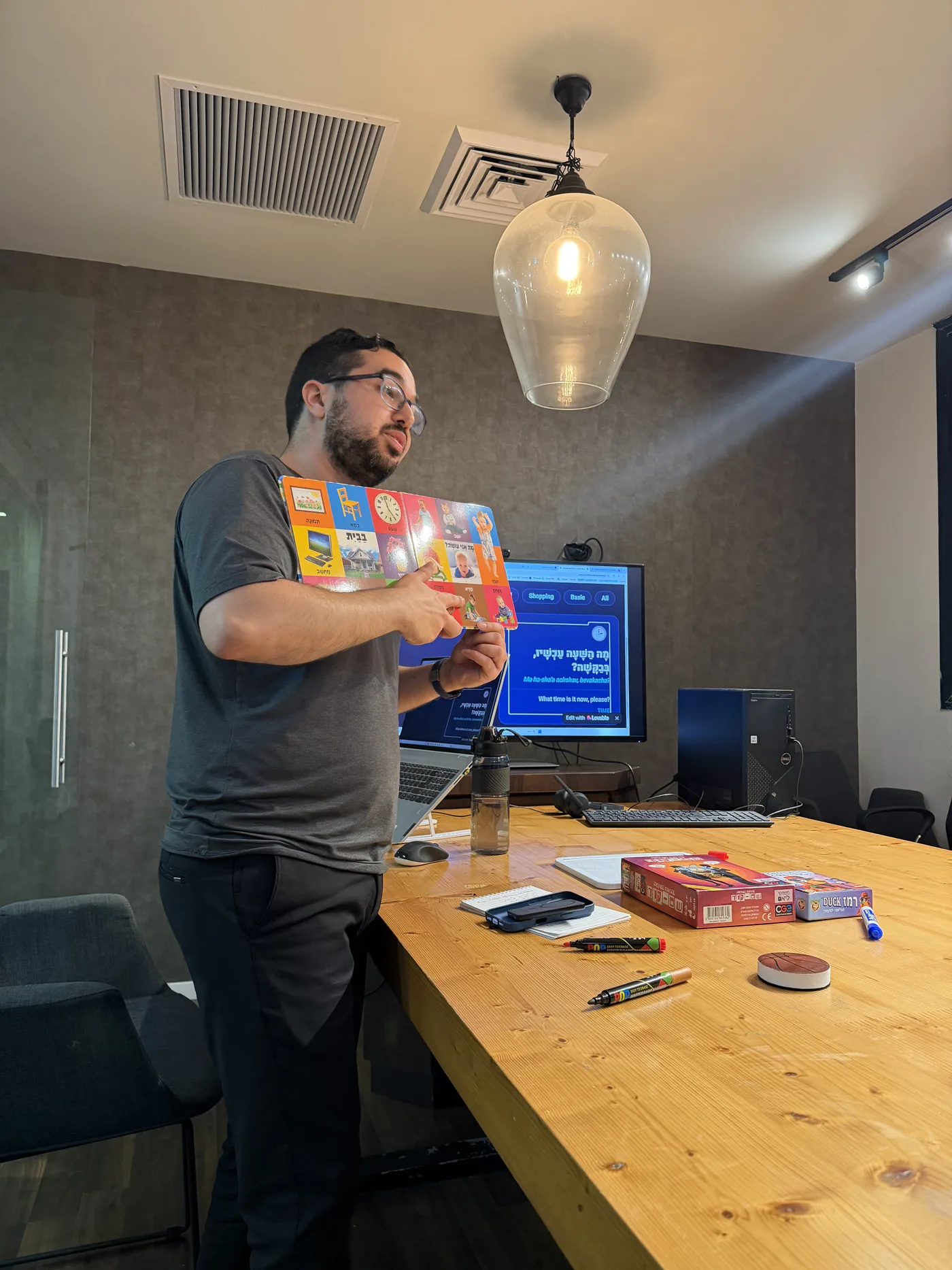 Itay teaching a Hebrew vocabulary lesson with a picture board, screen showing a Hebrish phrase card